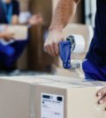Close-up of worker using tape dispenser while packing cardboard