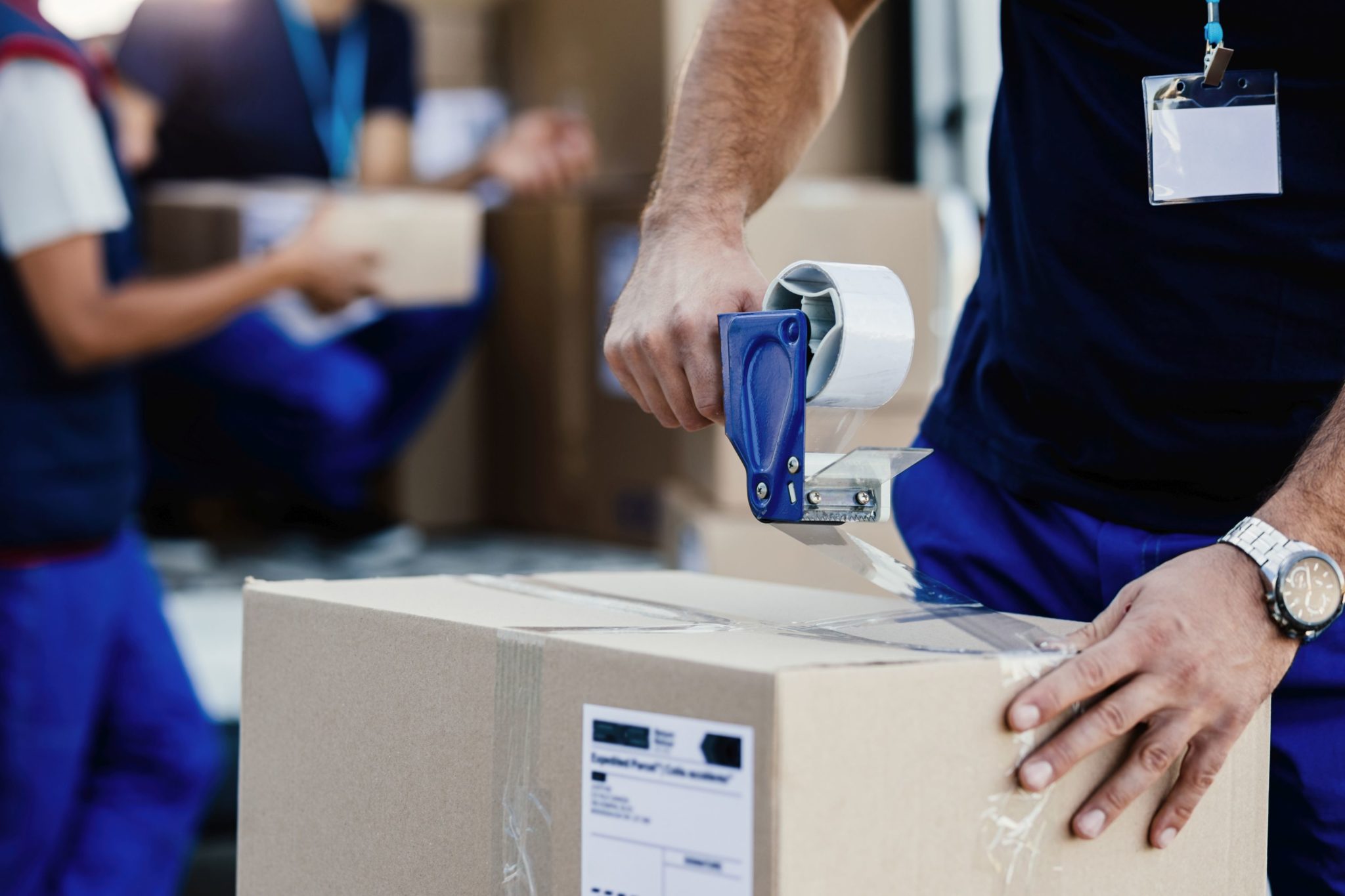 Close-up of worker using tape dispenser while packing cardboard